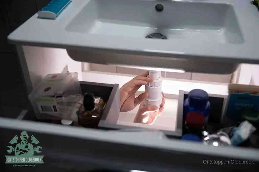 Een pompfles met zeep boven een wastafel, de heet water en afwasmiddel-methode om een vetprop in de afvoer los te maken in Oldebroek