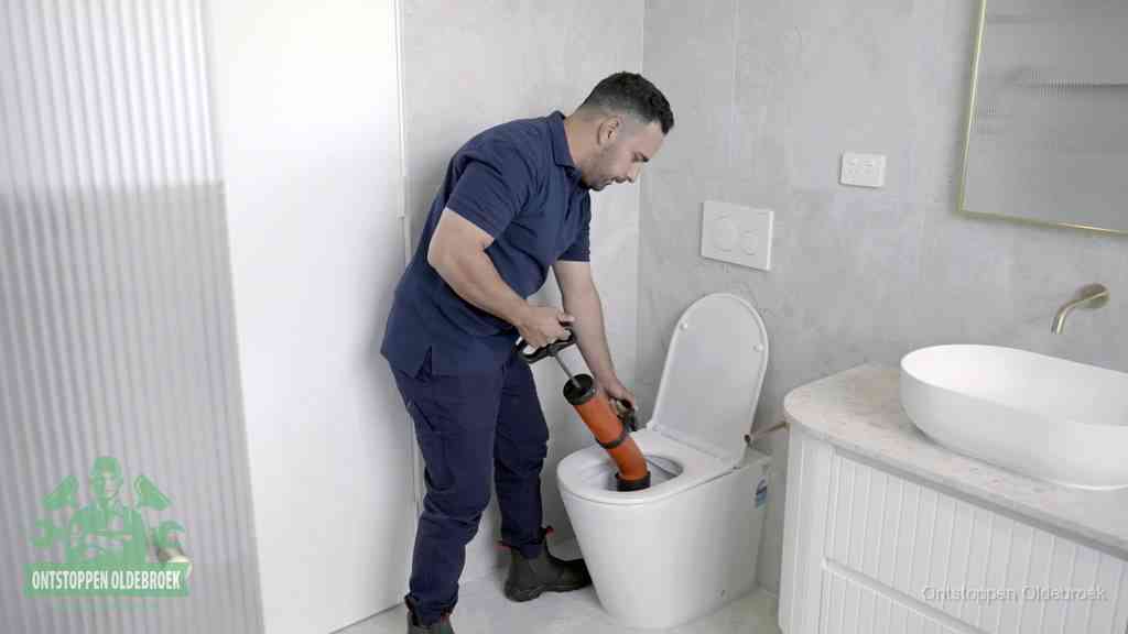 Een monteur buigt over een wandcloset en duwt met de hand een persluchtontstopper in de toiletpot om de verstopping handmatig los te maken in Oldebroek