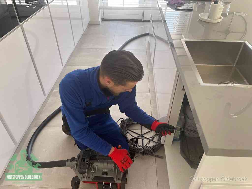 Een monteur ontstopt de keukenafvoer onder de spoelbak met een elektrische veermachine in Oldebroek