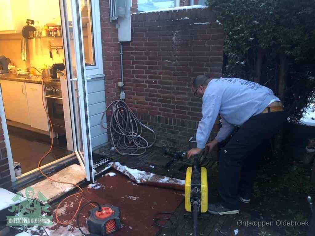 Een monteur werkt buiten bij een open riool-/grondput met een elektrische ontstoppingsmachine om een verborgen afvoerprobleem op te sporen in Oldebroek