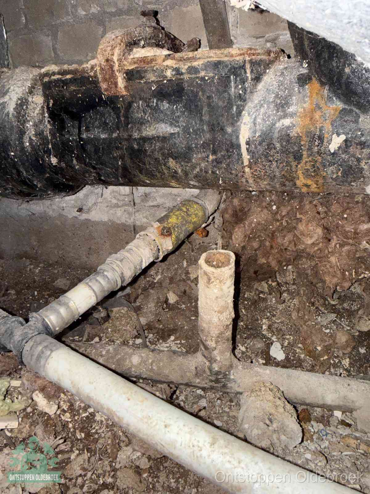 Een dikke zwarte hoofdrioolbuis met roest- en kalkaanslag in een kruipruimte, oorzaak van terugkerende structurele afvoerproblemen in Oldebroek