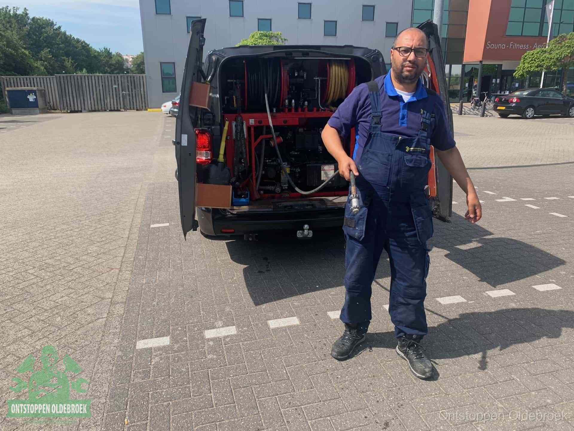 Een monteur bij zijn bestelbus met een hogedruk- en rioolreinigingsunit, klaar om de oorzaak van terugkerende wc-verstoppingen aan te pakken in Oldebroek