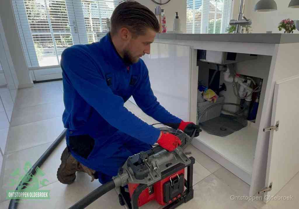 Een monteur voert een professionele elektrische ontstoppingsmachine in de afvoer onder de spoelbak tijdens het gootsteen ontstoppen in Oldebroek