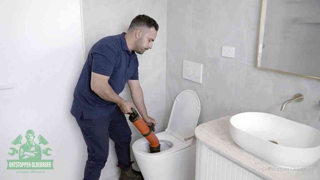 Een man gebruikt een handmatige luchtdruk-ontstopper in een modern betegeld toilet om zelf de wc te ontstoppen in Oldebroek